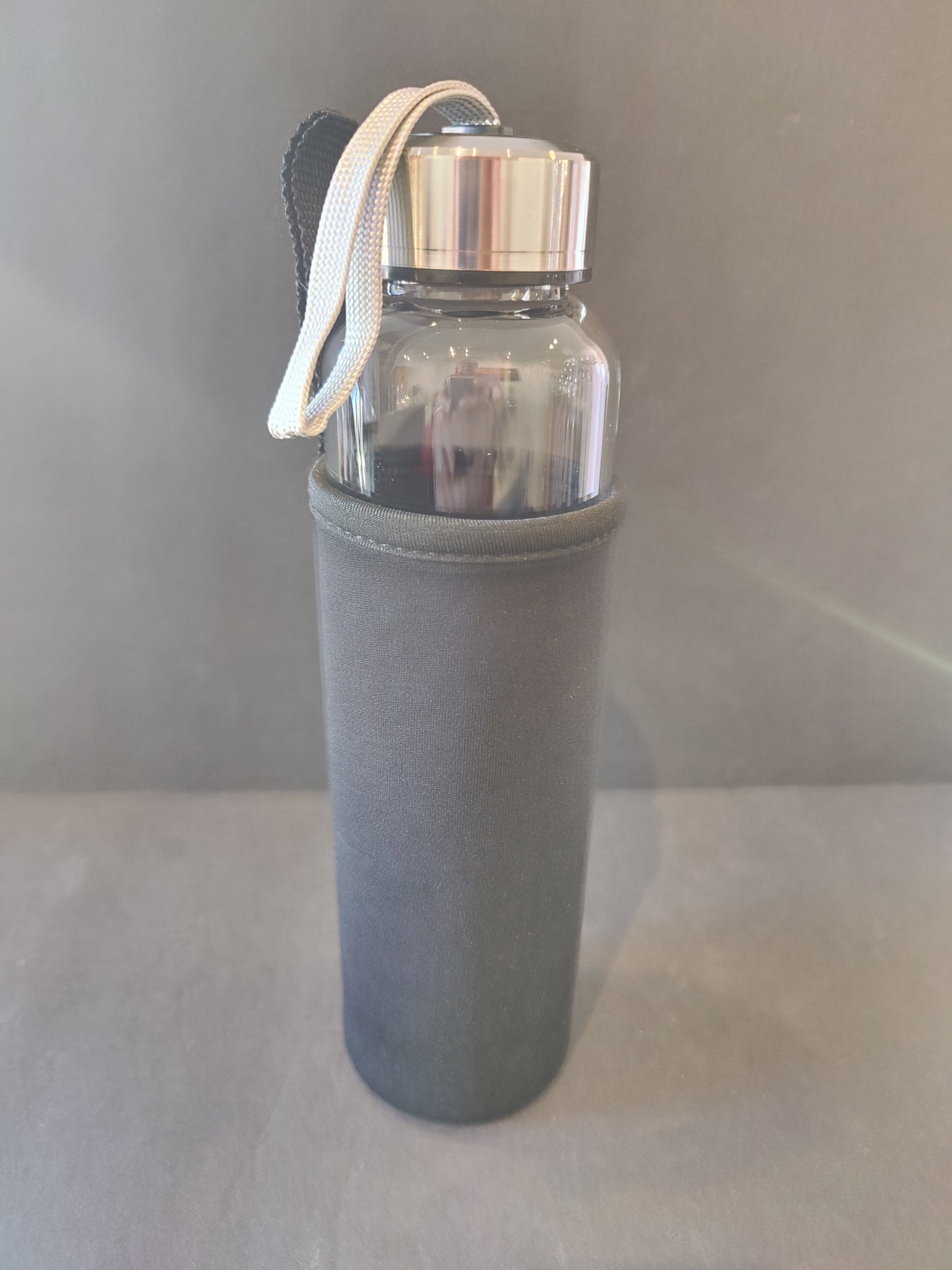 A crystal infused glass water bottle with a stainless steel cap and gray insulation sleeve standing upright against a neutral backdrop. — for Carpe Diem Dream