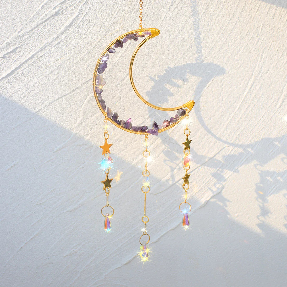 An amethyst crystal moon suncatcher with a gold crescent frame, purple stone chips, and hanging prism drops displayed in warm natural sunlight casting soft shadows and subtle rainbow reflections. — for Carpe Diem Dream