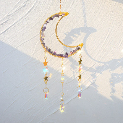 An amethyst crystal moon suncatcher with a gold crescent frame, purple stone chips, and hanging prism drops displayed in warm natural sunlight casting soft shadows and subtle rainbow reflections. — for Carpe Diem Dream