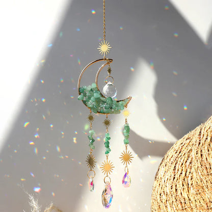 A green aventurine crystal moon suncatcher with a gold crescent frame, polished green stone chips, and hanging prism drops displayed in bright natural sunlight with vivid rainbow reflections and soft shadows. — for Carpe Diem Dream