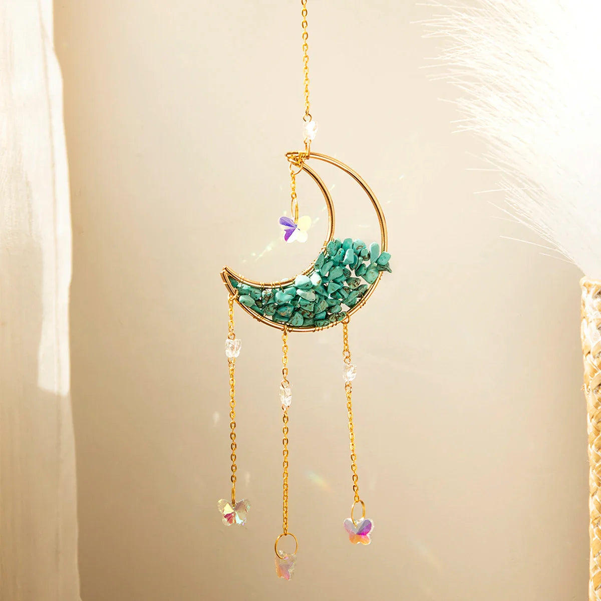 A green aventurine crystal moon suncatcher with a gold crescent frame, vibrant green stone chips, and hanging prism drops displayed in warm natural sunlight with soft shadows and subtle rainbow reflections. — for Carpe Diem Dream