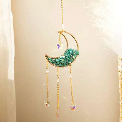 A green aventurine crystal moon suncatcher with a gold crescent frame, vibrant green stone chips, and hanging prism drops displayed in warm natural sunlight with soft shadows and subtle rainbow reflections. — for Carpe Diem Dream