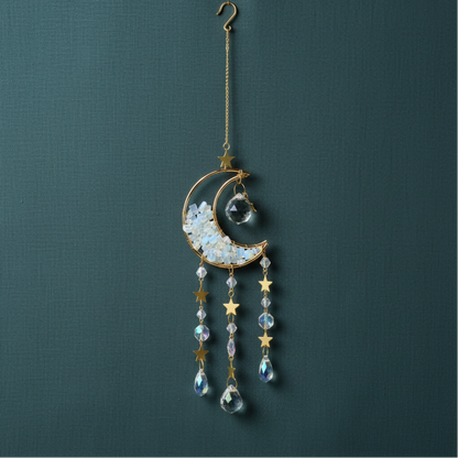 A crystal moon suncatcher with gold crescent moon, star accents, and hanging prism crystals displayed against a muted teal linen background. — for Carpe Diem Dream