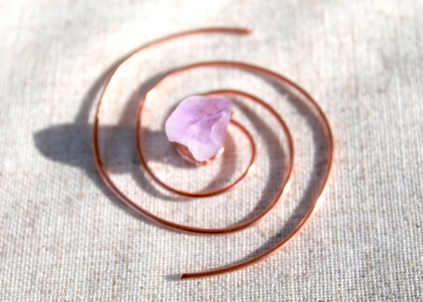 Amethyst copper spiral crystal water charger displayed on textured natural linen fabric. — for Carpe Diem Dream