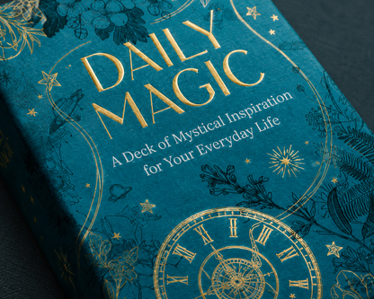Close-up detail of the Daily Magic deck cover featuring celestial clock artwork, botanical illustrations, and gold foil typography by Maia Toll. — for Carpe Diem Dream