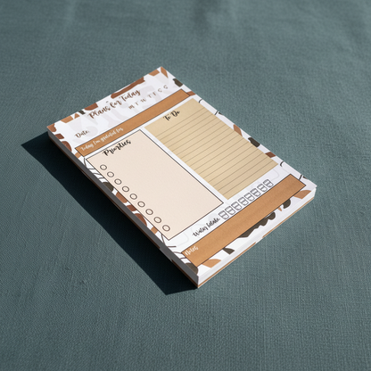 Angled close-up view of a minimalist 4x6 daily planning sticky notepad with priority and checklist sections on a muted teal textured surface in soft natural light. — for Carpe Diem Dream