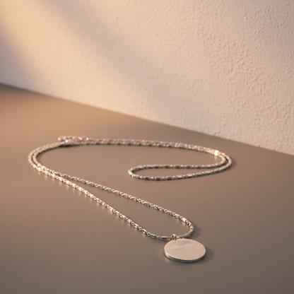 A circular defense pendant necklace with a white textured disc and silver chain arranged on a neutral matte surface with soft angled lighting and a textured wall backdrop. — for Carpe Diem Dream