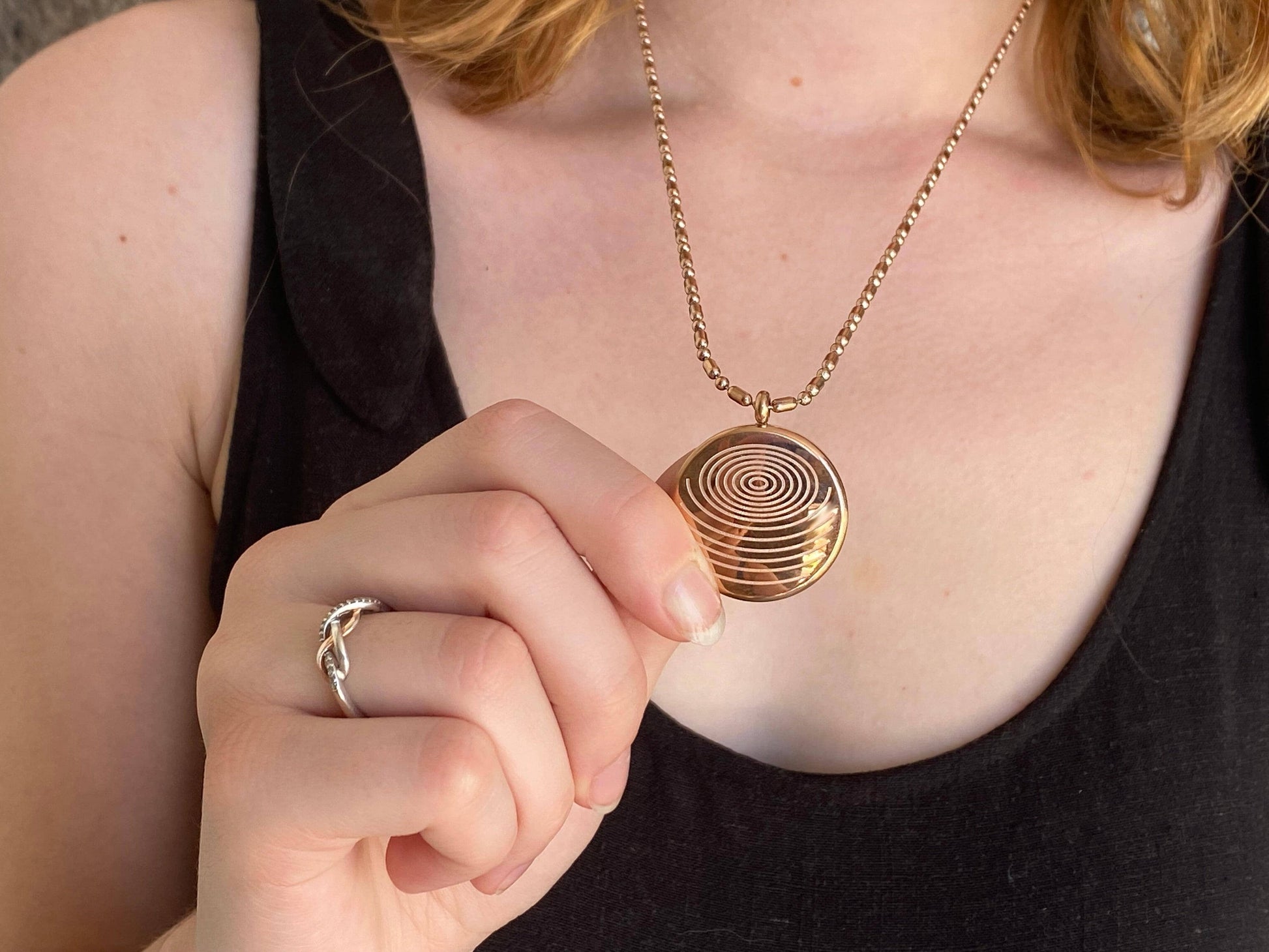 A person holding a circular gold defense pendant necklace against their chest, showing the textured spiral design and chain in a real-wear setting. — for Carpe Diem Dream