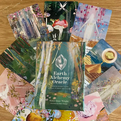An Earth Alchemy Oracle Deck box surrounded by illustrated cards arranged in a circular spread on a wooden surface. — for Carpe Diem Dream