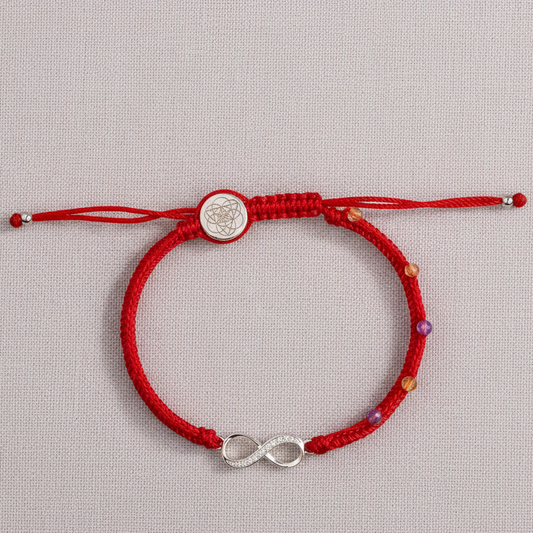 Red string bracelet with sterling silver infinity charm displayed on a textured neutral backdrop under soft natural lighting. — for Carpe Diem Dream