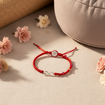 Red string bracelet with a silver infinity charm resting on a textured meditation mat beneath soft natural lighting. — for Carpe Diem Dream