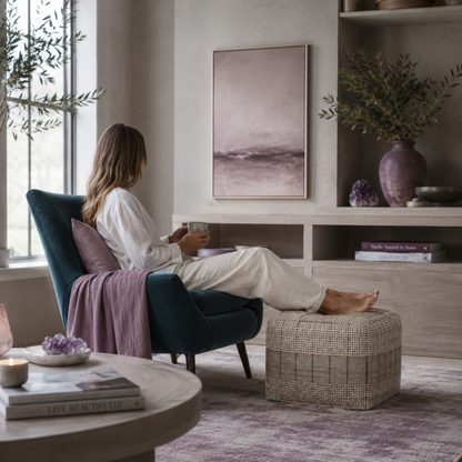 Woman relaxing with her feet on the Elmer handwoven jute and cotton square pouf in a calm living room with dark teal and mauve accents. — for Carpe Diem Dream