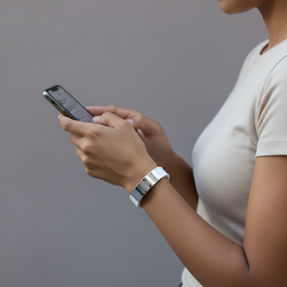 White EMF defense bracelet worn on the wrist while using a smartphone, illustrating everyday use around devices in a clean minimal setting. — for Carpe Diem Dream