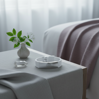 White EMF defense bracelet placed on a soft draped surface beside a small vase and crystal in a serene bedroom spa setting with gentle natural light. — for Carpe Diem Dream