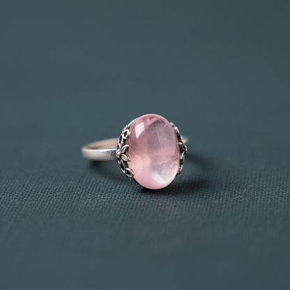 A close-up view of The Emotional Release Ring highlighting the polished rose quartz stone set in a silver band against a deep teal background. — for Carpe Diem Dream