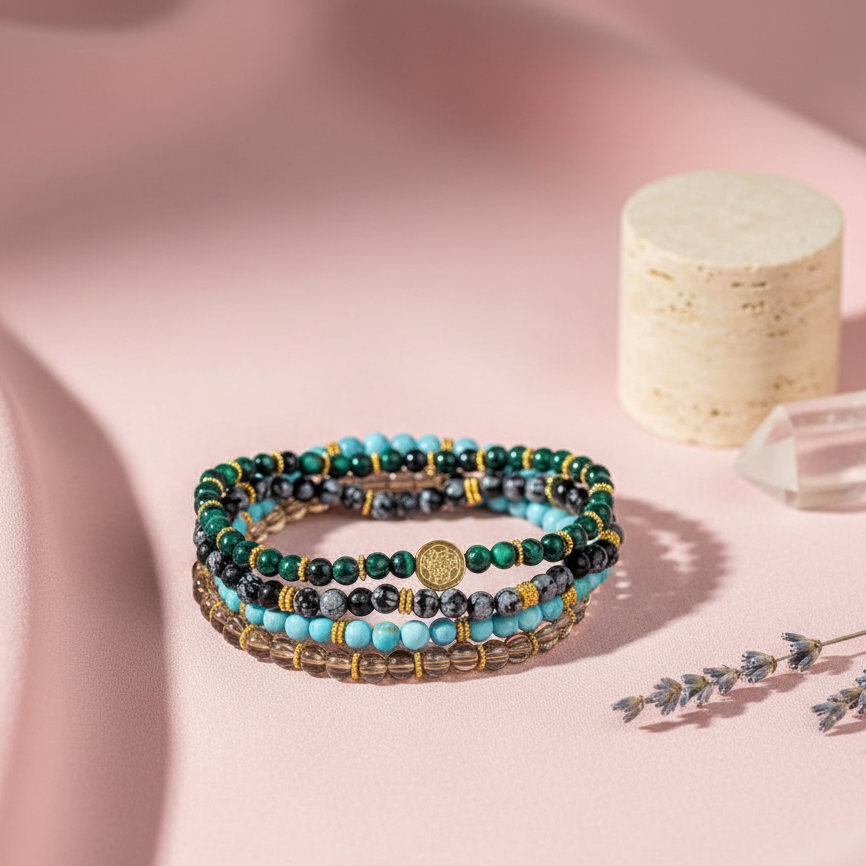 A stacked set of four crystal bracelets featuring turquoise, malachite, smoky quartz, and snowflake obsidian arranged on a soft pink surface with a candle, crystal point, and dried botanicals. — for Carpe Diem Dream