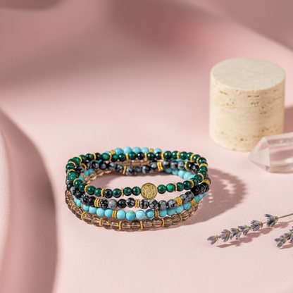 A stacked set of four crystal bracelets featuring turquoise, malachite, smoky quartz, and snowflake obsidian arranged on a soft pink surface with a candle, crystal point, and dried botanicals. — for Carpe Diem Dream