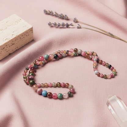 A beaded tourmaline necklace arranged in a loose oval on soft pink fabric with dried lavender, a stone block, and crystal accents. — for Carpe Diem Dream