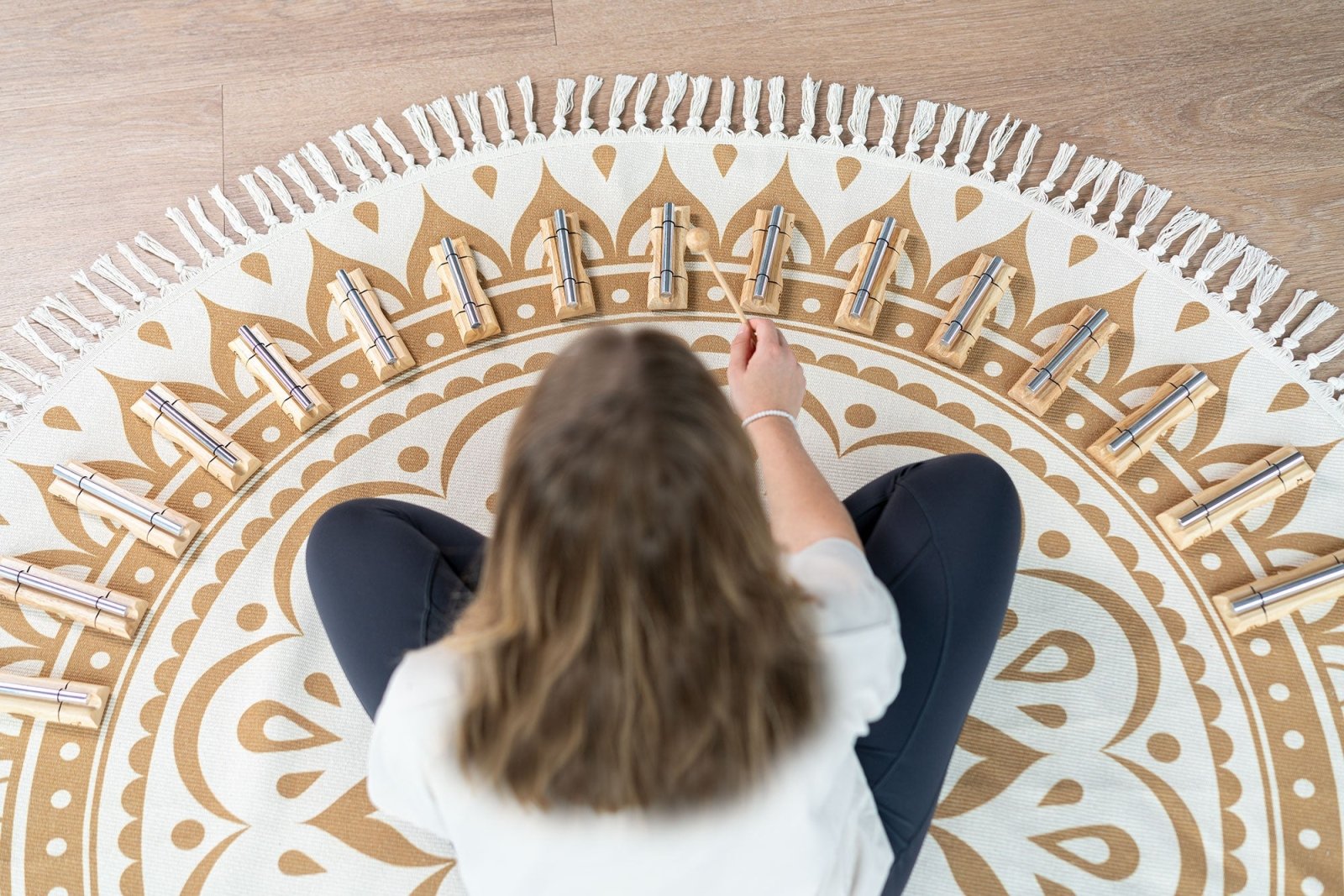 Person seated on a patterned meditation rug playing a circular layout of sixteen planetary energy chimes with wooden beaters. — for Carpe Diem Dream
