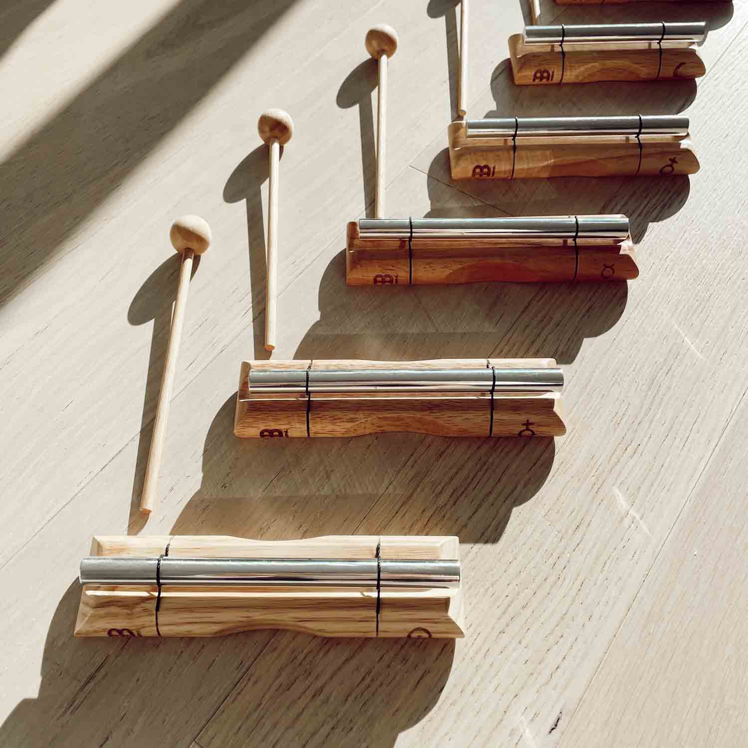 Planetary chakra energy chimes and wooden mallets arranged in a row on a sunlit wooden surface. — for Carpe Diem Dream