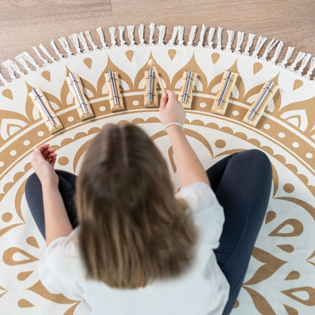 Person seated on a patterned meditation mat playing a set of chakra energy chimes arranged in a semicircle. — for Carpe Diem Dream