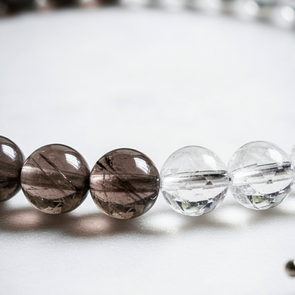 Close-up of Smoky Quartz and Clear Quartz gemstone beads from the anklet displayed on soft white surface.
 — for Carpe Diem Dream