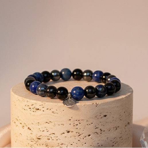 Lapis Lazuli, Onyx, and Hematite gemstone bracelet displayed upright on a travertine pedestal against a soft peach backdrop. — for Carpe Diem Dream