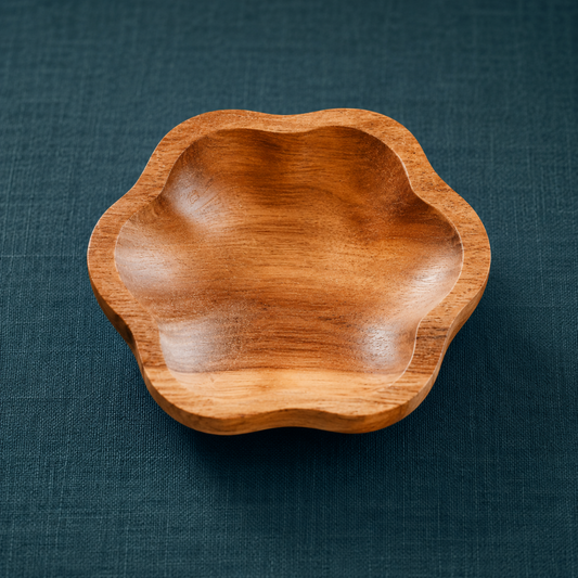 Single hand-carved teak catch all dish with natural wood grain and flower-shaped edges on a dark teal textured linen backdrop. — for Carpe Diem Dream