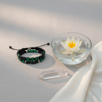 A malachite and black tourmaline bracelet set arranged on a wide white ritual dish beside a glass bowl holding a floating lotus flower, illuminated by warm directional light with draped silk and small crystal. — for Carpe Diem Dream
