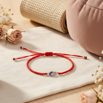 Red string bracelet with a silver Hamsa charm and amethyst resting on soft meditation props with gentle natural lighting and neutral tones. — for Carpe Diem Dream