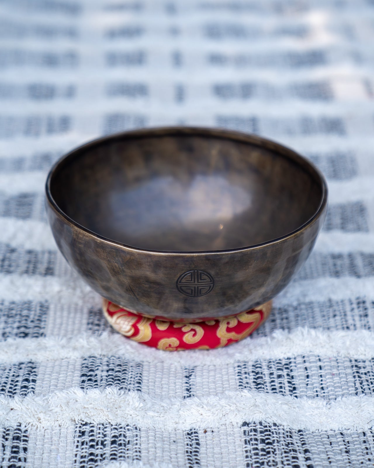 Root chakra Tibetan singing bowl with engraved full moon symbol resting on a red embroidered cushion. — for Carpe Diem Dream