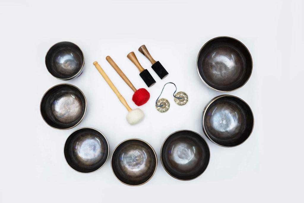 Top view of seven chakra singing bowls arranged in a circular formation with embroidered cushions on a white background. — for Carpe Diem Dream
