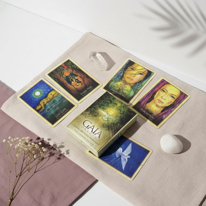 A Gaia Oracle Cards deck is arranged on layered fabric with crystals and botanical elements in a softly lit lifestyle setting. — for Carpe Diem Dream