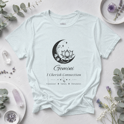 Gemini Moon I Cherish Connection zodiac T-shirt in Heather Ice Blue with black moon-inspired lotus, floral, and celestial artwork and Expression, Variety, Stimulation text, styled in a cool-toned studio botanical flat lay with eucalyptus, lavender, crystals, and ceramic accents. — for Carpe Diem Dream