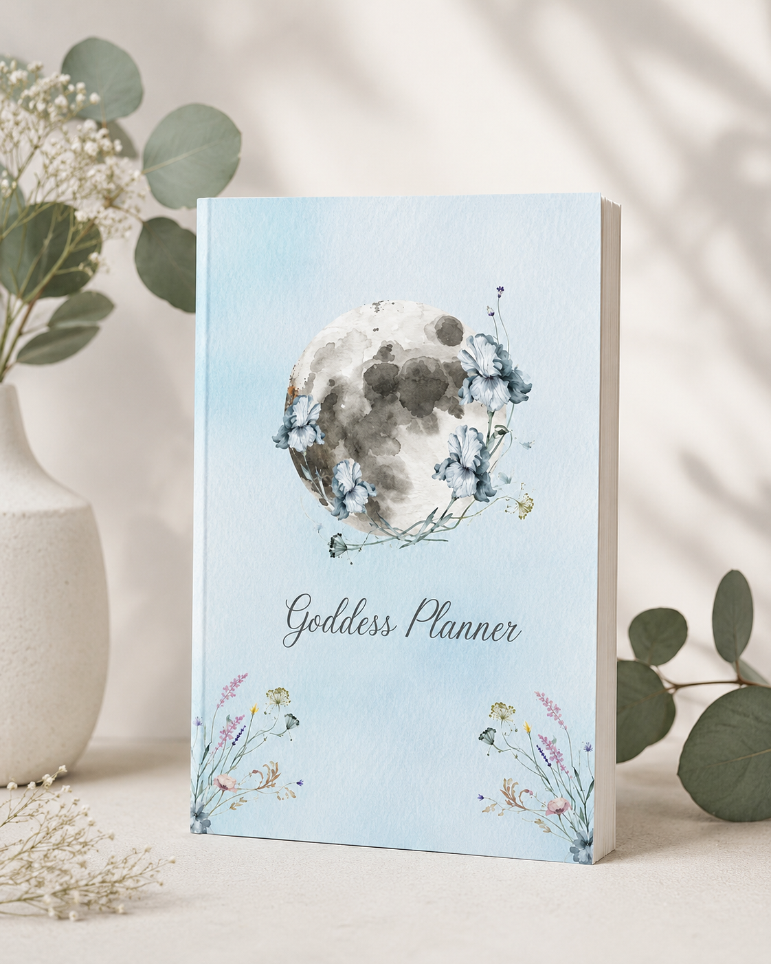 Goddess Planner paperback displayed in a botanical-inspired sanctuary setting with layered textiles, fresh greenery, and moon-inspired accents, supporting lunar reflection, self-care rituals, mindful planning, and intentional living. — for Carpe Diem Dream