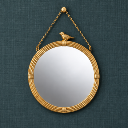 Round gold hanging wall mirror with decorative bird accent, ribbed resin frame, and gold chain against a dark teal textured linen background.