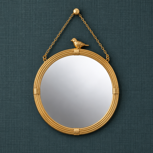 Round gold hanging wall mirror with decorative bird accent, ribbed resin frame, and gold chain against a dark teal textured linen background.
