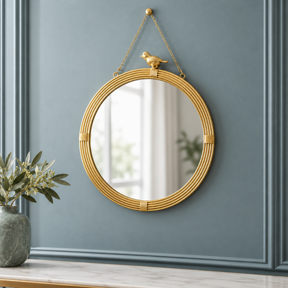 Gold hanging wall mirror with decorative bird accent, ribbed resin frame, and gold chain displayed on a cool blue-gray paneled wall with subtle botanical accents.
