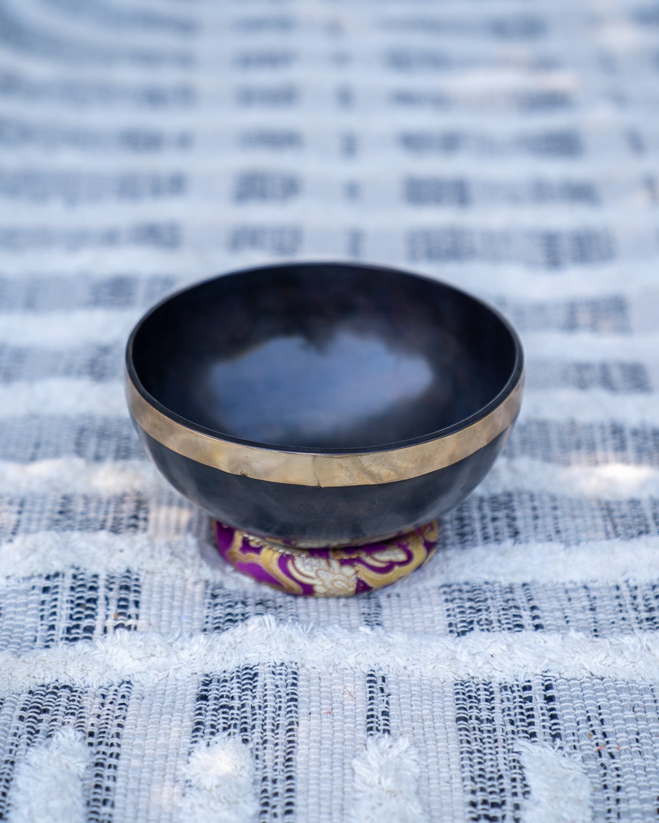 Single gold mandala Tibetan singing bowl resting on a purple embroidered cushion on a textured woven fabric background. — for Carpe Diem Dream