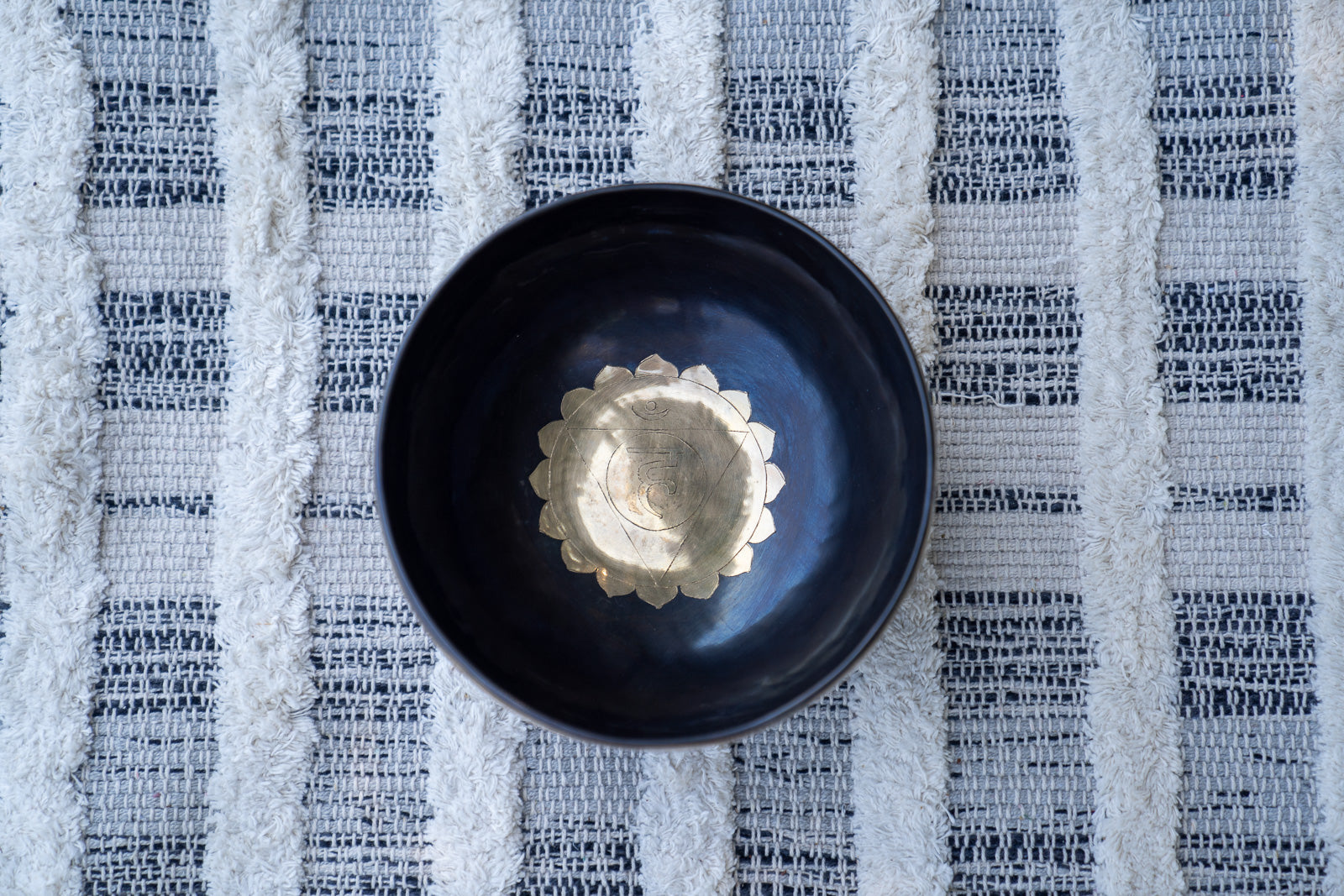 Top view of a gold mandala Tibetan singing bowl showing the throat chakra Sanskrit symbol resting on textured white and blue fabric. — for Carpe Diem Dream