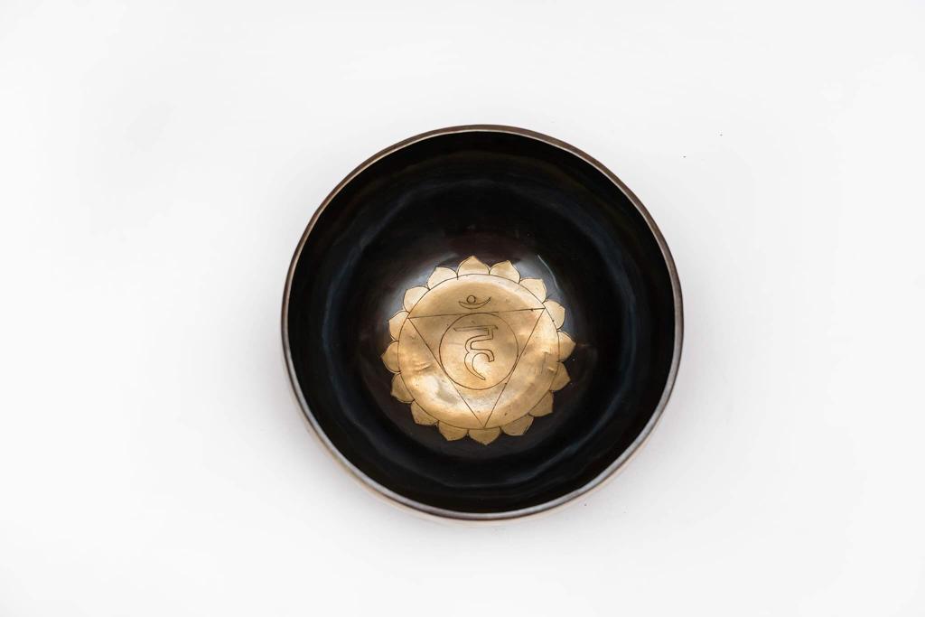 Top view of a black singing bowl with a gold mandala emblem on a white background. — for Carpe Diem Dream