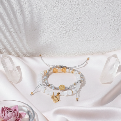 A set of crystal bracelets featuring citrine, moonstone, and labradorite beads with gold spacer accents and a gold hand of hamsa charm arranged on soft pink fabric with clear quartz points. — for Carpe Diem Dream