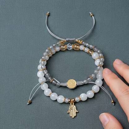 A set of crystal bracelets featuring citrine, moonstone, and labradorite beads with gold spacer accents and a gold hand of hamsa charm shown beside a hand for size reference on a muted teal background. — for Carpe Diem Dream