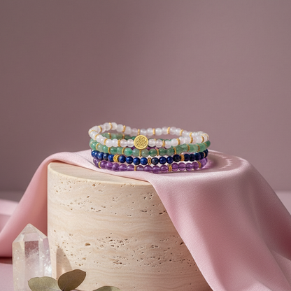 Stack of multicolored gemstone luck bracelets displayed on round pedestal with pink silk fabric and clear quartz cluster. — for Carpe Diem Dream