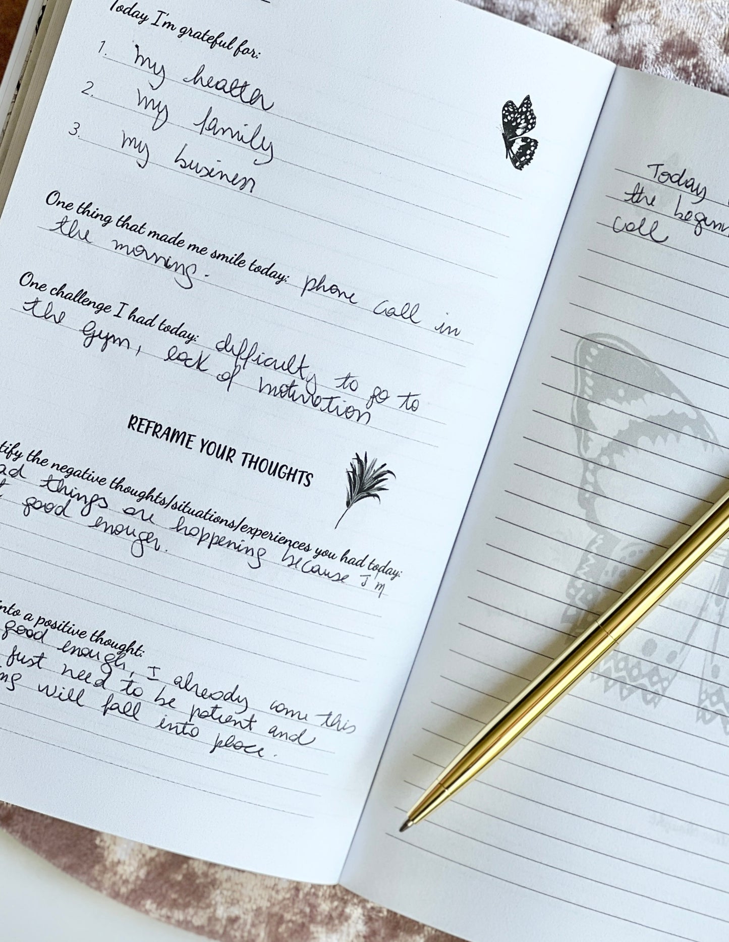 Open spread of Gratitude Daily Journal showing completed guided prompts on the left page and lined writing page with leaf watermark on the right, styled with a gold pen on a blush velvet surface — for Carpe Diem Dream