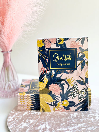 Front cover of floral Gratitude Daily Journal in glossy softcover format displayed on a white surface with stacked copies behind it — for Carpe Diem Dream