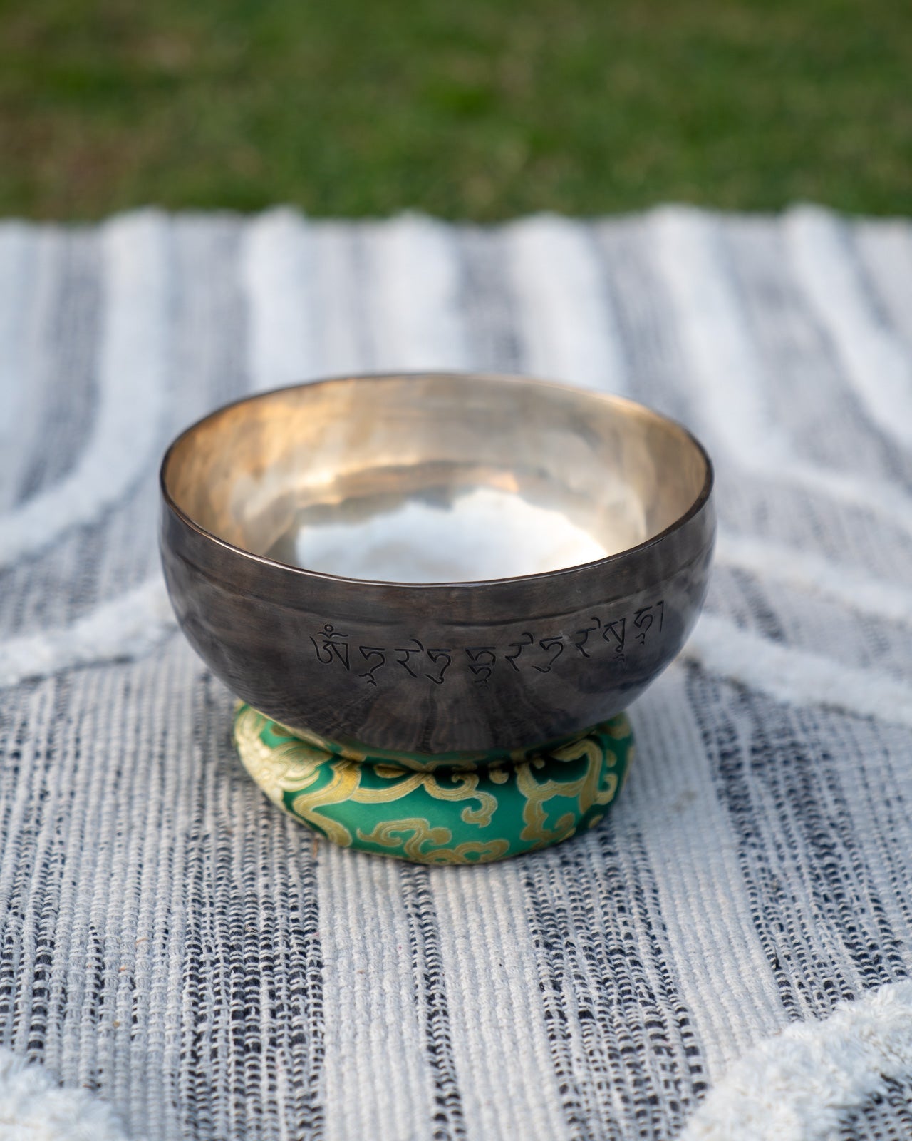 Back view of a Heart Chakra New Moon singing bowl showing engraved Tibetan mantra resting on a green cushion. — for Carpe Diem Dream