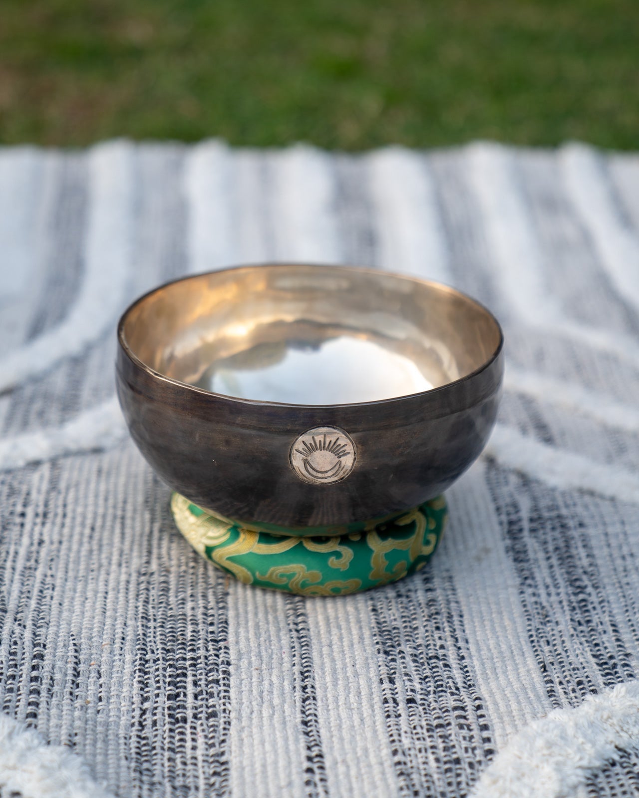 Front view of a Heart Chakra New Moon singing bowl with engraved sun and moon symbol resting on a green cushion. — for Carpe Diem Dream