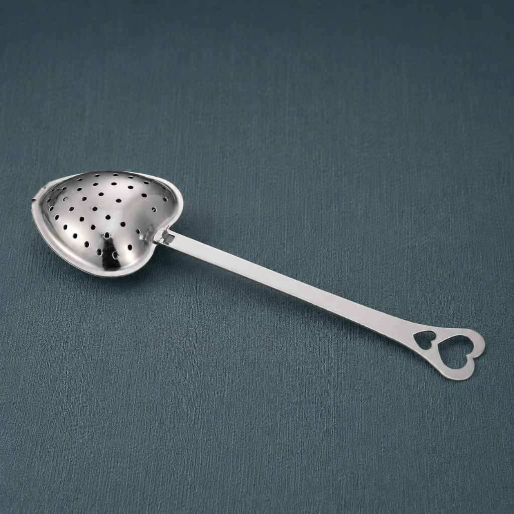 Heart Shaped Tea Infuser – authentic silver heart-shaped metal tea infuser displayed lying flat on a dark teal textured linen backdrop with matching linen surface, photographed in cool diffused daylight with soft natural shadows and premium commercial styling. The product remains the sole focal point with no props. — for Carpe Diem Dream