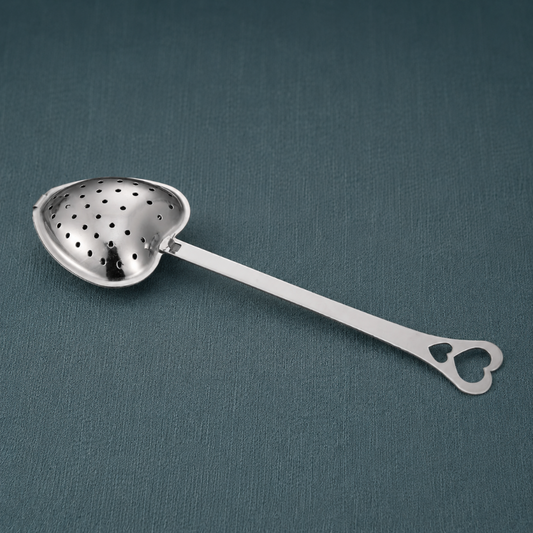 Heart Shaped Tea Infuser – authentic silver heart-shaped metal tea infuser displayed lying flat on a dark teal textured linen backdrop with matching linen surface, photographed in cool diffused daylight with soft natural shadows and premium commercial styling. The product remains the sole focal point with no props. — for Carpe Diem Dream